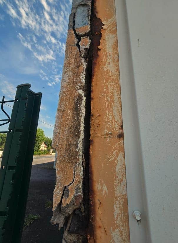 Poteau métallique d'angle avec corrosion avancée et enduit de façade éclaté